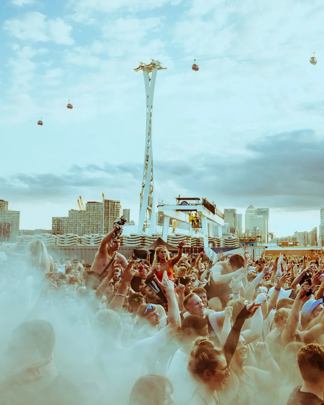 DnB Allstars Censored x 30Hz: London: Smoke-filled crowd, hands up, cable-car pylon and skyline under blue sky