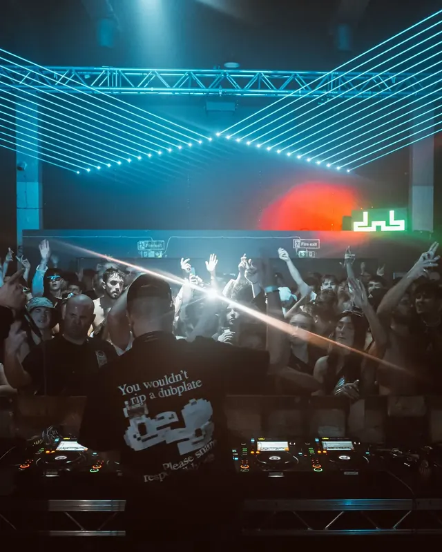 DnB Allstars Censored x 30Hz: London: Blue laser truss and dnb logo over hands-up crowd, DJ in foreground