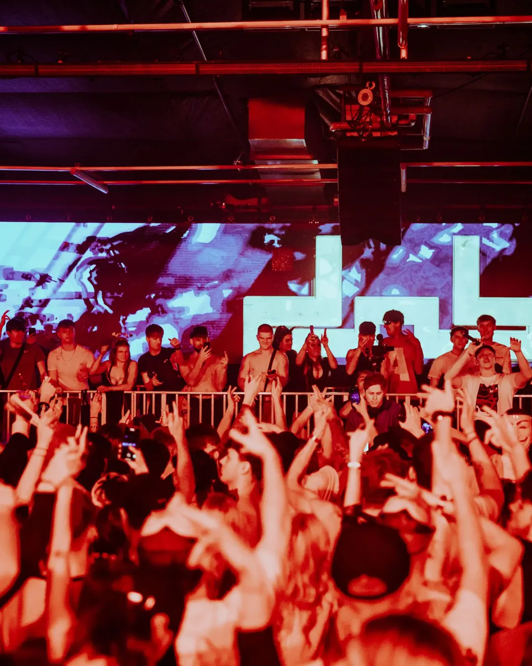 DnB Allstars Halloween: Bristol: Red-lit hands-up crowd before the glowing dnb logo screen, branded and energetic