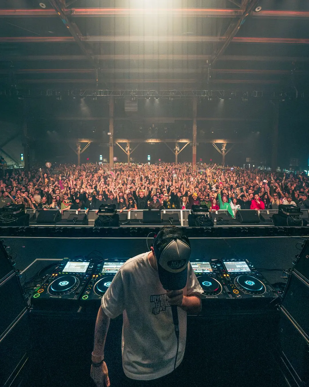 DnB Allstars: New York: Alternate pose at the booth, huge hazy crowd behind, face hidden by cap