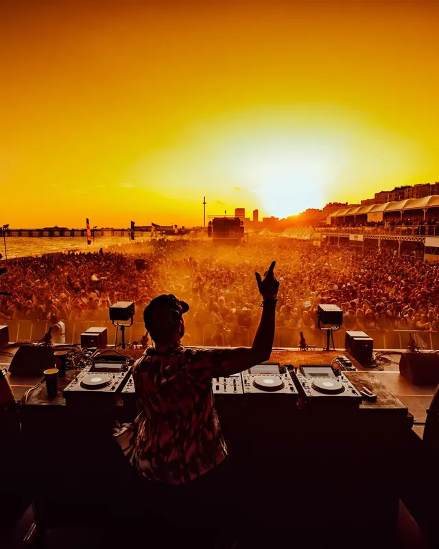 DnB Allstars On The Beach: Brighton: DJ arm up against blazing sunset, seafront crowd stretching away