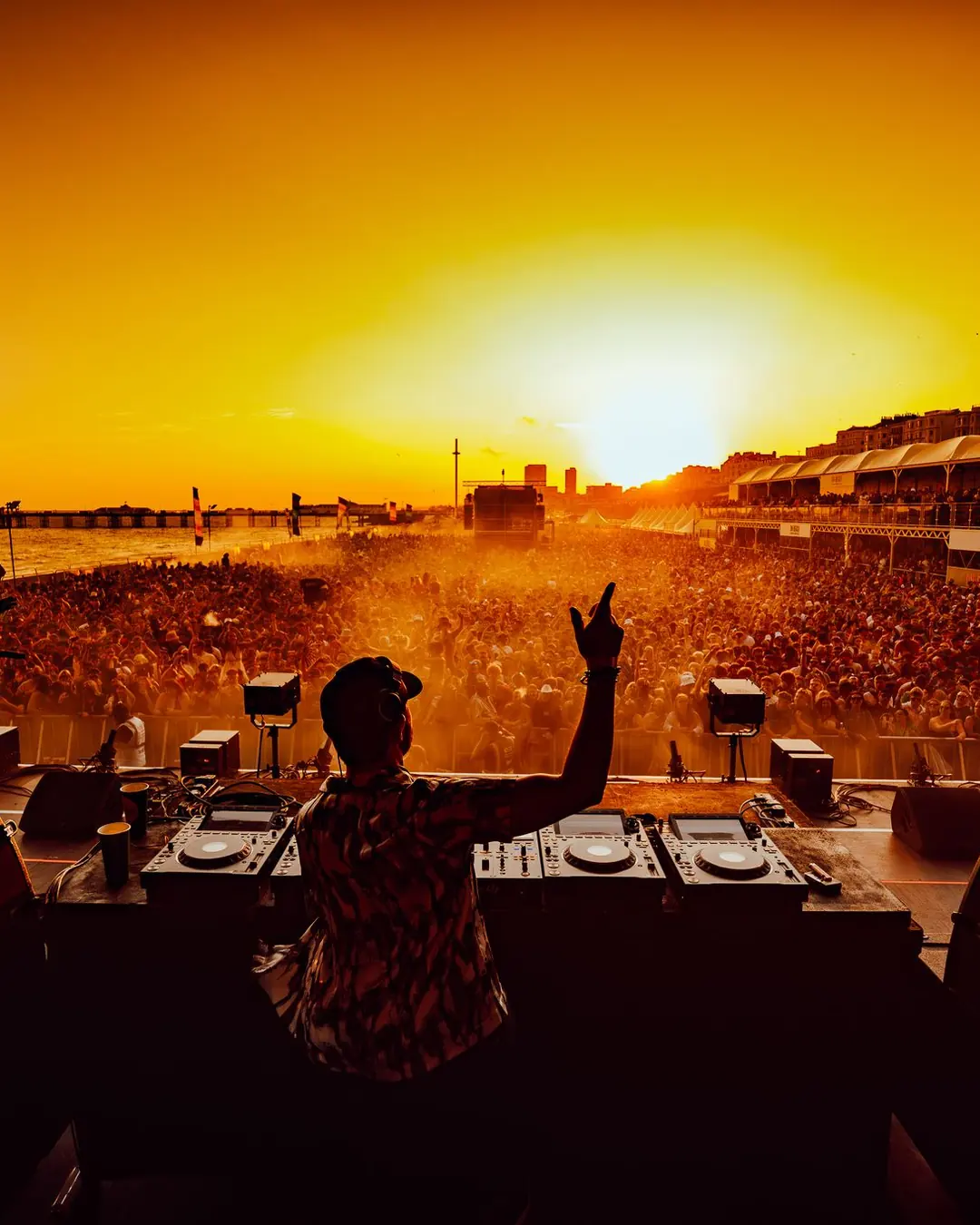 DnB Allstars On The Beach: Brighton: DJ arm up against blazing sunset, seafront crowd stretching away